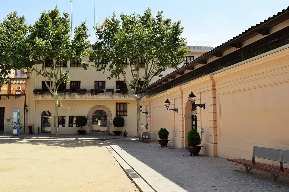 Fachada del Mercat Municipal d'Alella con árboles y plaza tranquila en el centro del pueblo